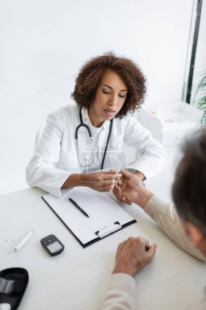 African american doctor checking hand of blurred patient with diabetes in clinic 