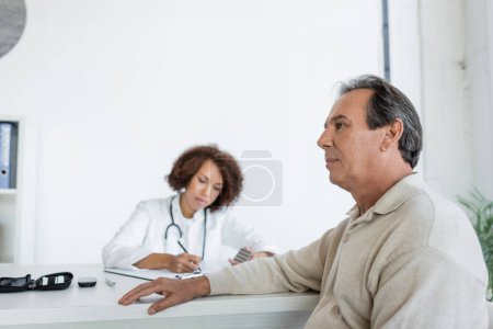Homme mûr avec diabète assis près flou afro-américain médecin en clinique 