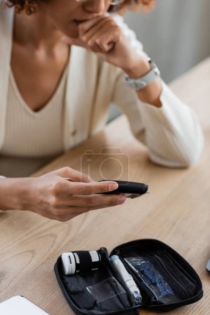 Cropped view of african american businesswoman checking blood sugar with glucometer in office 