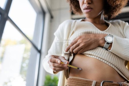 Niski kąt widzenia afrykańskiej bizneswoman robi wstrzyknięcie insuliny w ciało w biurze 