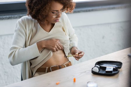 Afroamerykanka z cukrzycą wykonująca wstrzyknięcie insuliny w pobliżu apteczki w biurze 
