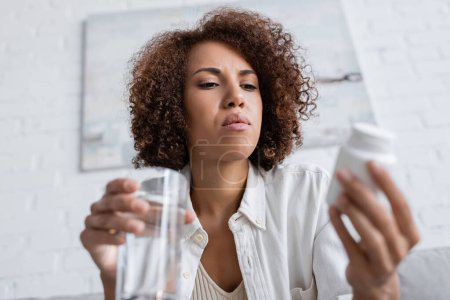 Low angle view of african american woman with diabetes holding blurred pills and water at home 