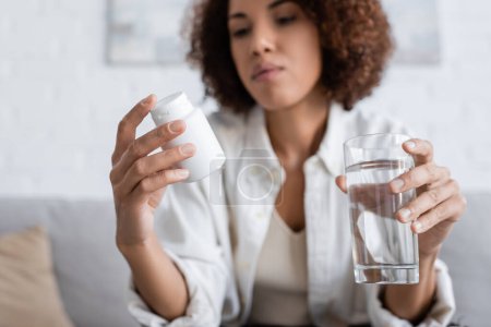Blurred african american woman with diabetes holding pills and water at home 