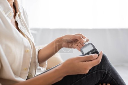 Cropped view of african american woman with diabetes using blurred glucometer at home 