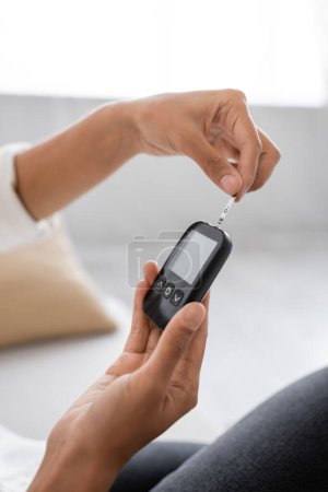 Cropped view of african american woman using glucometer while checking insulin at home 