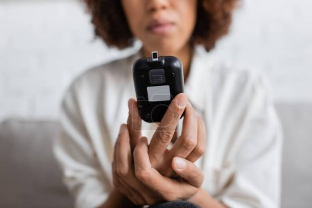 Ausgeschnittene Ansicht einer afrikanisch-amerikanischen Frau mit Diabetes, die ein Glukometer zu Hause hält
