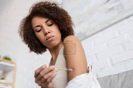 Vue à angle bas de la jeune femme afro-américaine diabétique faisant une injection d'insuline dans le bras dans le salon 