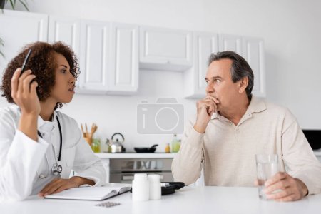 African american doctor talking to middle aged man with diabetes near notebook and pills at home 