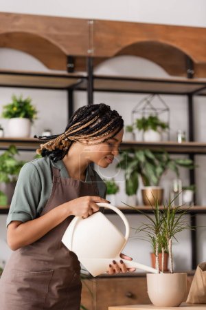 Photo for Side view of african american florist with dreadlocks watering tropical plant in flower shop - Royalty Free Image