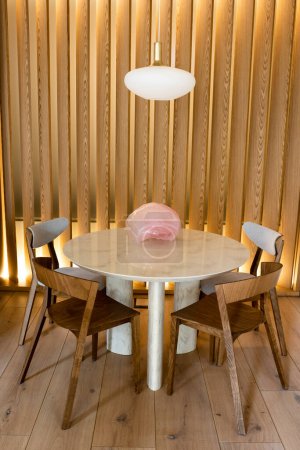 Foto de Decorative pink figurine on round dining table near wooden chairs and modern lamp - Imagen libre de derechos