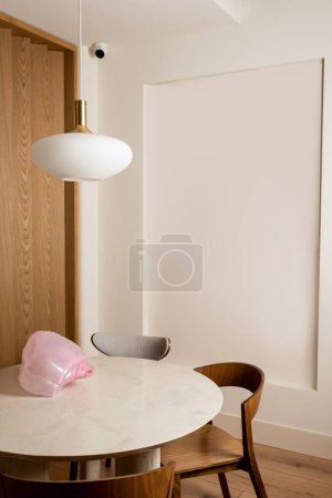 decorative pink figurine on round dining table near wooden chairs in hotel room with security camera 