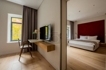 Téléchargez les photos : Flat tv screen near wooden desk and chair next to bedroom in hotel room - en image libre de droit