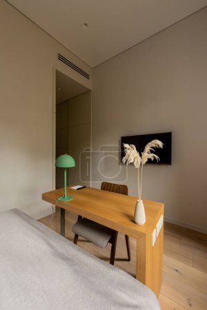 wooden desk and chair near tv flat screen on wall in hotel room 