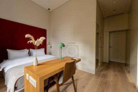 Foto de Wooden chair near table with lamp and comfortable bed in hotel room - Imagen libre de derechos