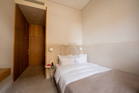 Photo for Book and telephone on bedside table near comfortable bed with pillows in hotel room - Royalty Free Image