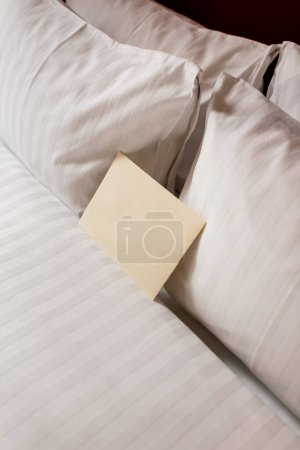 high angle view of blank envelope on white and clean bedding in hotel room 