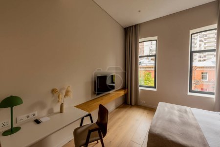 Photo pour Wooden chair near workspace and flat tv screen on wall in bedroom of hotel - image libre de droit