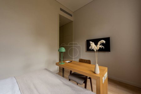 Photo for Wooden desk and tv with blank screen on wall near bed in room of hotel - Royalty Free Image