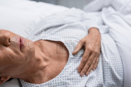 Téléchargez les photos : Cropped view of sick senior man lying on blurred bed in hospital ward - en image libre de droit