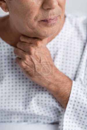 Cropped view of sick senior man touching neck in hospital