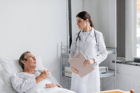 Sick elderly patient talking to doctor with paper folder in hospital