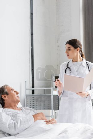 Arzt mit Papiermappe im Gespräch mit älterer Patientin in Klinik