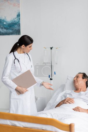 Brünette Ärztin mit Papiermappe im Gespräch mit älterer Patientin in Klinik