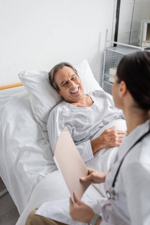 Positive Seniorin sieht verschwommenen Arzt mit Papiermappe auf Krankenhausstation 