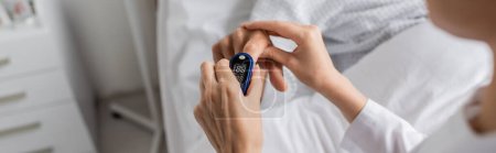 Cropped view of blurred doctor wearing pulse oximeter on finger of senior patient in hospital, banner 