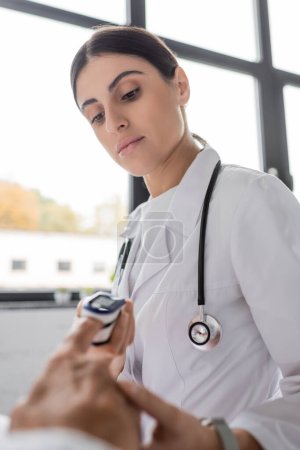 Téléchargez les photos : Doctor looking at pulse oximeter on finger of senior patient in hospital ward - en image libre de droit