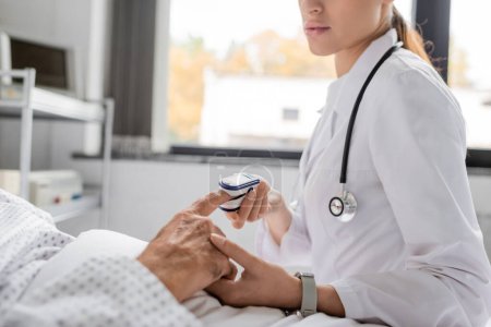 Ausgeschnittene Ansicht eines Arztes mit Pulsoximeter am Finger eines älteren Mannes auf der Krankenhausstation 