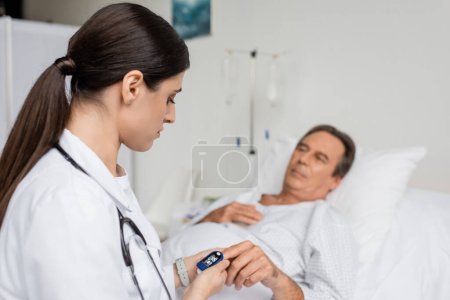 Téléchargez les photos : Doctor looking at pulse oximeter on finger of senior patient in hospital - en image libre de droit