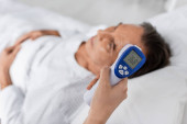 Doctor holding pyrometer near blurred elderly patient in clinic  mug #632105304