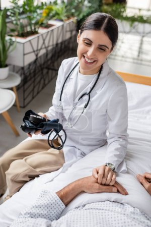Lächelnder Arzt mit Tonometer-Berührung der Hand eines älteren Patienten in Klinik 