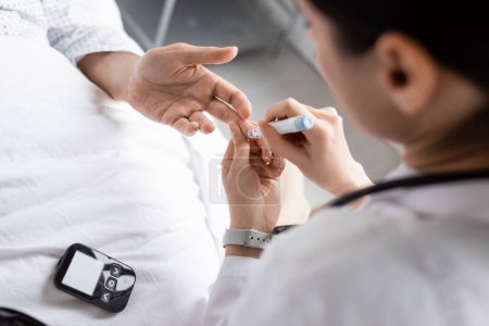 Verschwommener Arzt hält Lanzenstift in der Nähe der Hand eines Diabetes-Patienten auf Krankenhausstation 