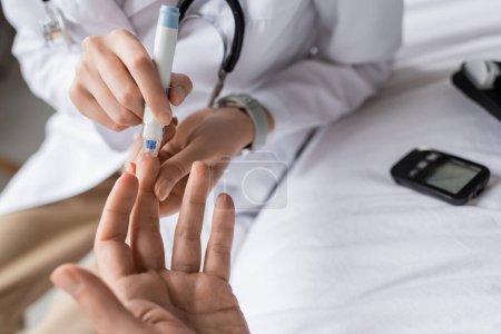 Cropped view of doctor with lancet pen checking blood sugar of patient in clinic 