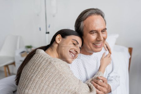 Foto de Smiling woman hugging father in patient gown in hospital - Imagen libre de derechos