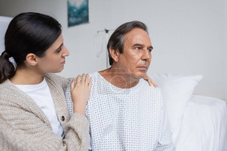 Photo for Woman hugging upset dad in patient gown in clinic - Royalty Free Image