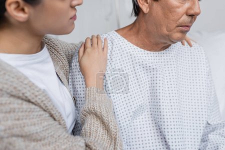 Ausgeschnittene Ansicht von Frau umarmt Senior-Vater in Patientenkleid auf Krankenhausstation 