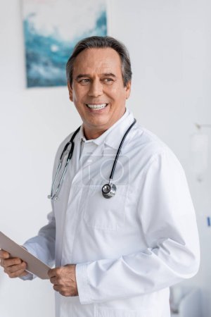 Positive senior doctor holding paper folder in clinic 