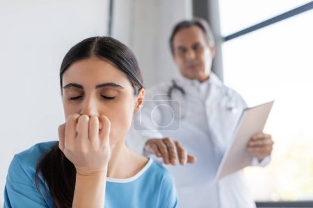 Dissatisfied patient closing eyes near blurred doctor in hospital ward 