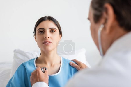 Verschwommener Arzt hält Stethoskop in der Nähe der Brust des Patienten in Klinik 