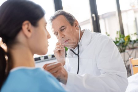Älterer Arzt untersucht Lungen verschwommener Patientin auf Krankenhausstation 