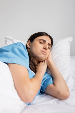 Kranke brünette Patientin im Kleid schläft, während sie in Klinik auf Bett liegt 