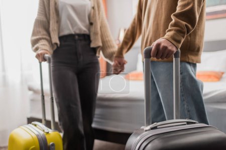 partial view of blurred couple with luggage holding hands in hotel apartments