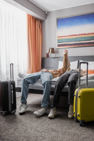 young couple of travelers holding hands and showing triumph gesture near suitcases in hotel bedroom