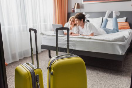 selective focus of suitcases near young travelers watching movie on laptop in modern hotel bedroom