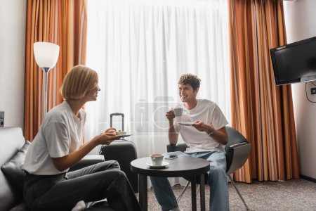 Photo for Happy young couple looking at each other while having breakfast in modern hotel suite - Royalty Free Image