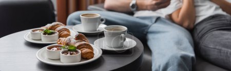 tasty croissants with jam and chocolate paste near coffee cups and cropped couple on blurred background, banner