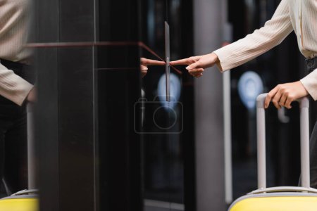 Photo pour Cropped view of woman with travel bag pressing elevator call button in hotel - image libre de droit